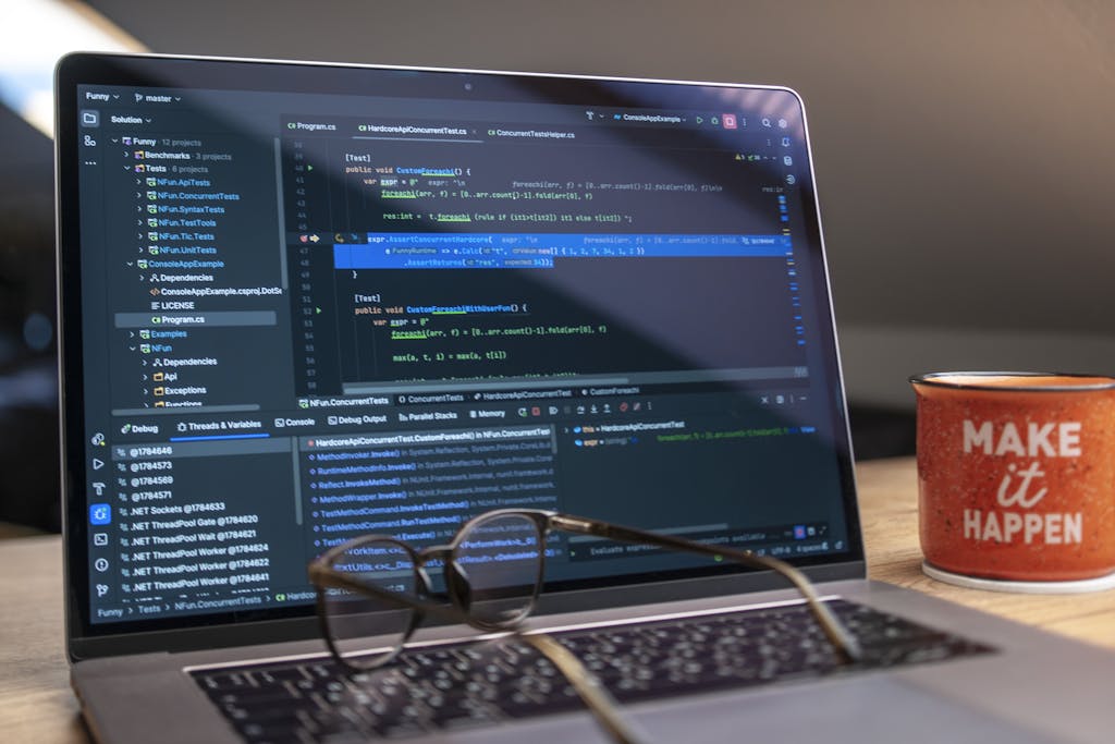 A laptop displaying code editor with a motivational mug that reads 'Make It Happen' on a workspace.