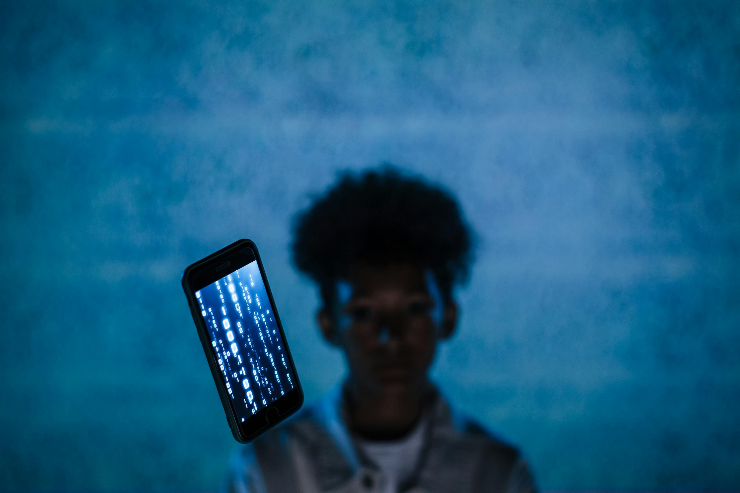 A smartphone with digital code floats in focus, blurring the person behind, suggesting digital immersion.
